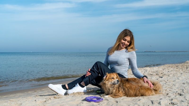 Woman enjoying a sunny day at Kołobrzeg beach with her dog, capturing a perfect seaside moment.