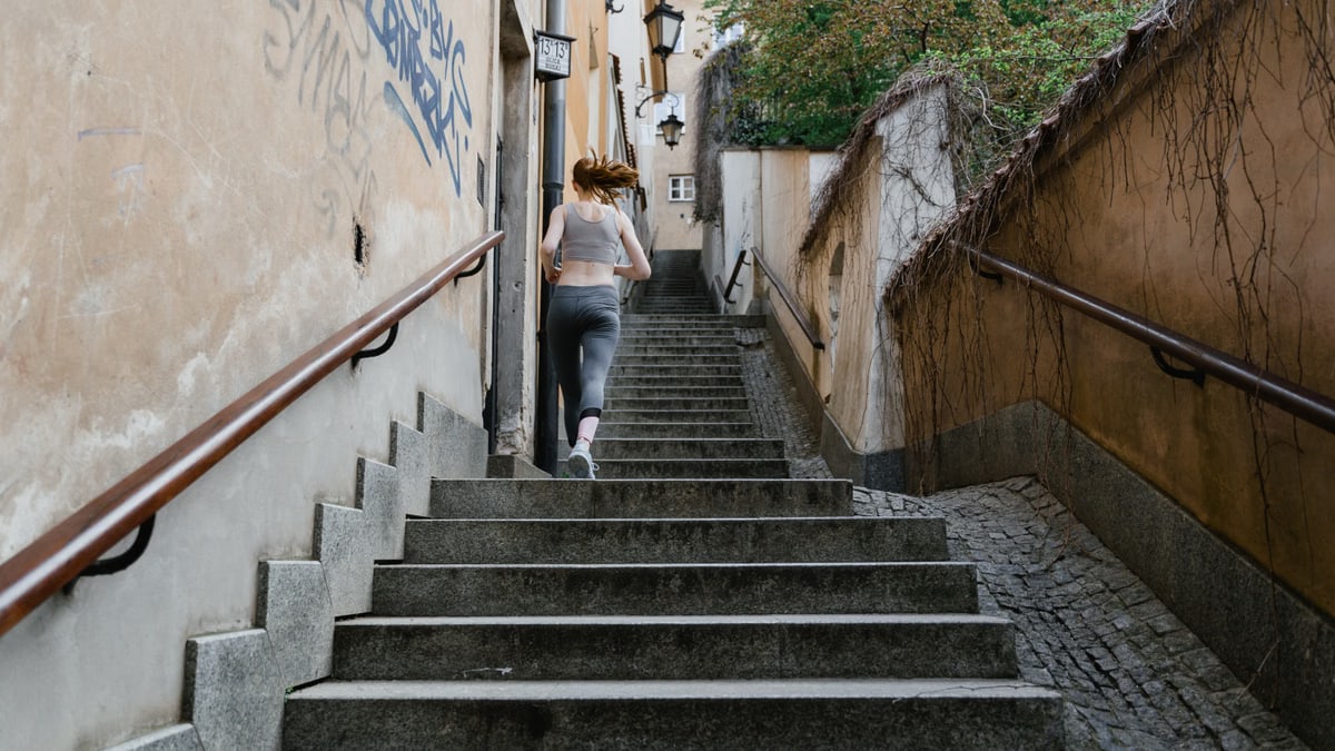 A woman exercising by running up a staircase in an outdoor urban setting.